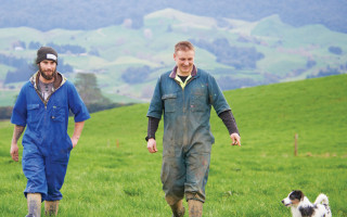 Two men walk through a field with a dog by their side