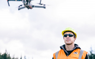 A man wearing a helmet and a hi-vis vest operates a drone