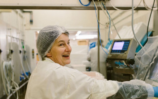 A lady wearing a hairnet smiles as she packs fish into boxes