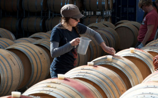 A woman stands between a number of wine barrels